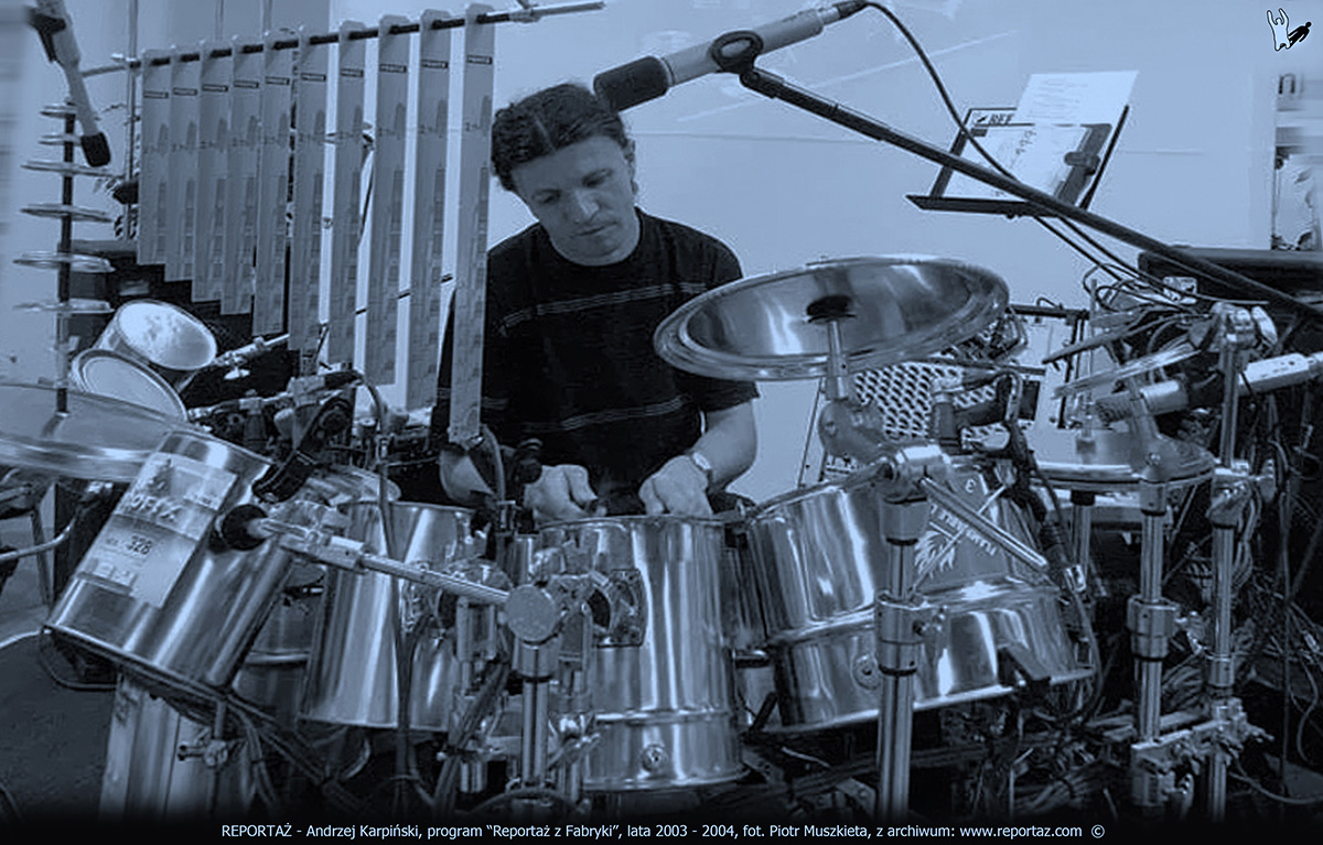 Andrzej Karpiński podczas programu Reportaż z Fabryki. Perkusja zbudowana z puszek po farbach na tle sampli z produkcji farb.